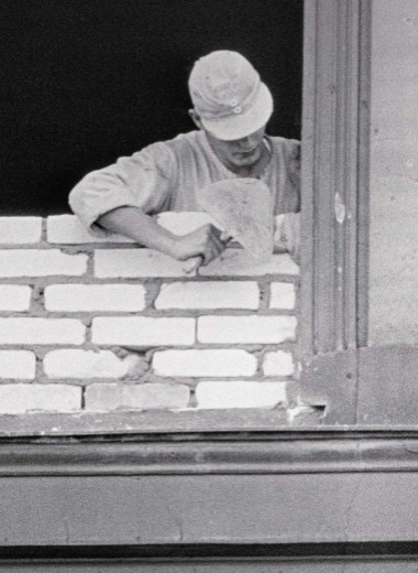 Восточноберлинский рабочий заделывает окно, выходящее на Западный Берлин