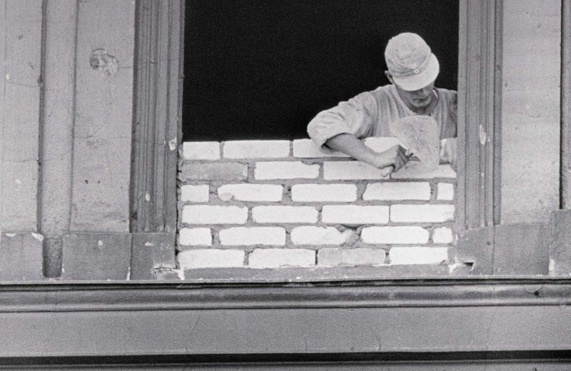 Восточноберлинский рабочий заделывает окно, выходящее на Западный Берлин